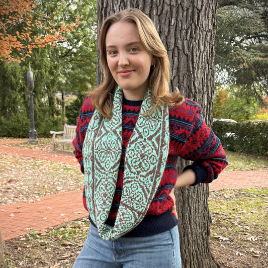 Person wearing a patterned scarf and colorful sweater standing next to a tree outdoors.